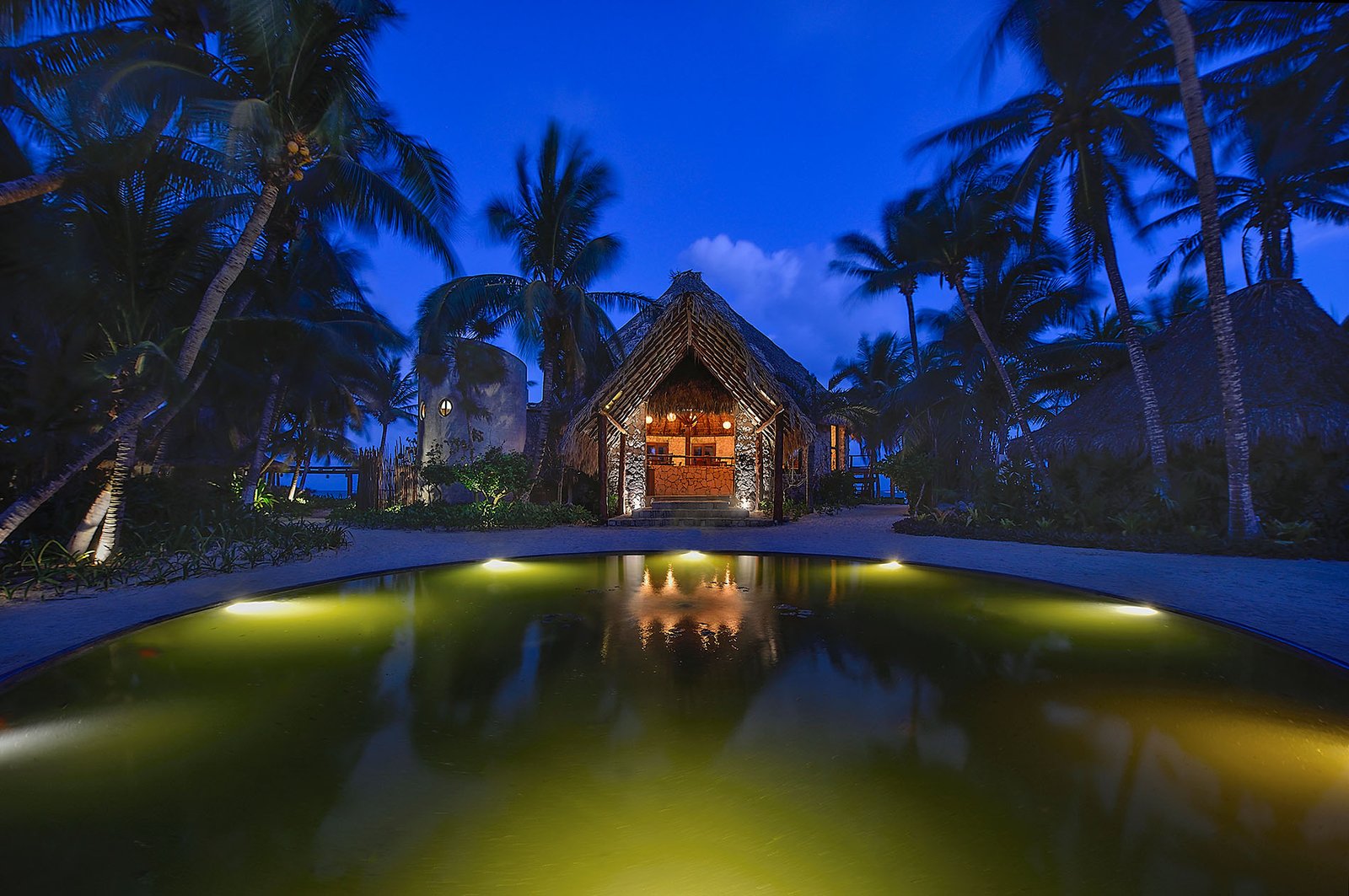 Vista frontal de la entrada del Hotel Maya Tulum durante la noche, con luces cálidas y ambiente acogedor