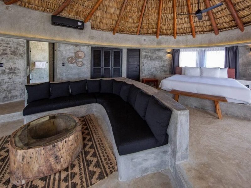 Interior de la habitación Emperor en Maya Tulum, con un sillón grande, mesa de madera y cama detrás